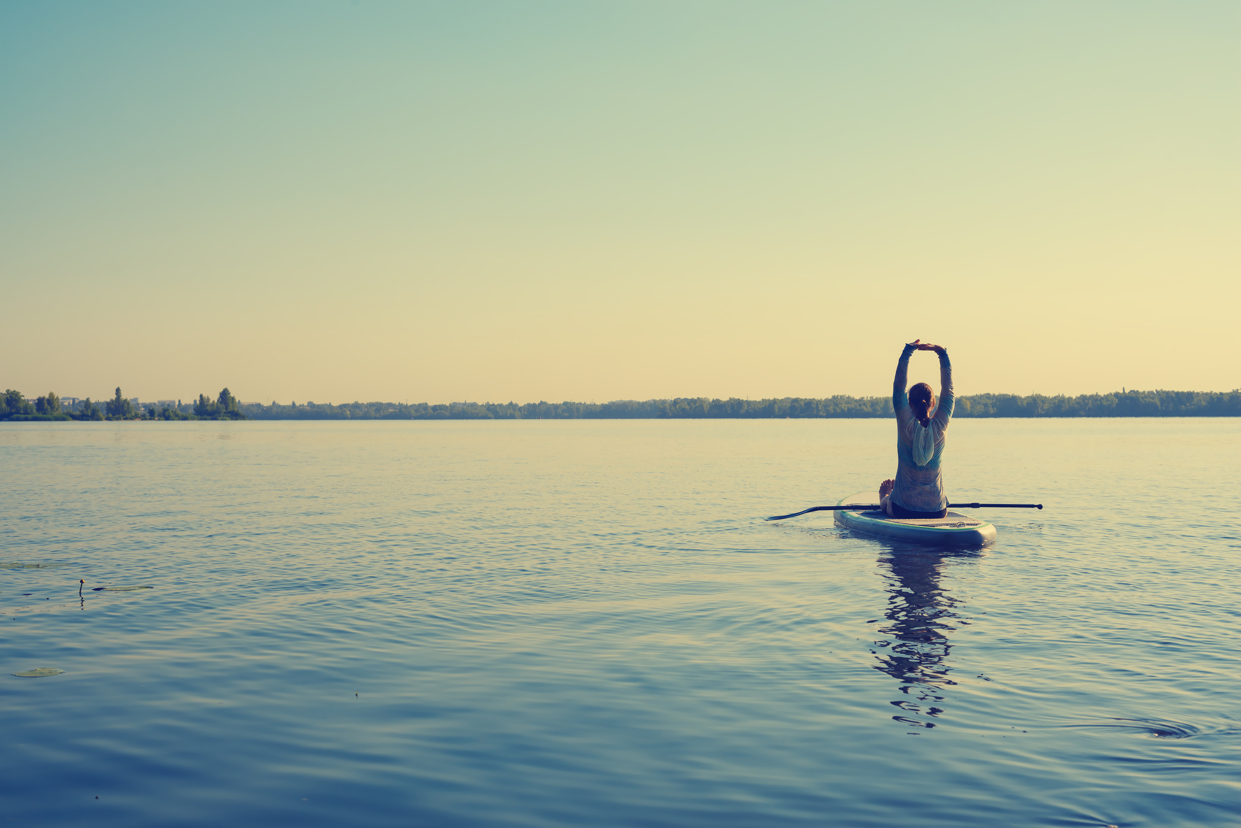Female practicing yoga on a SUP board during sunny morning